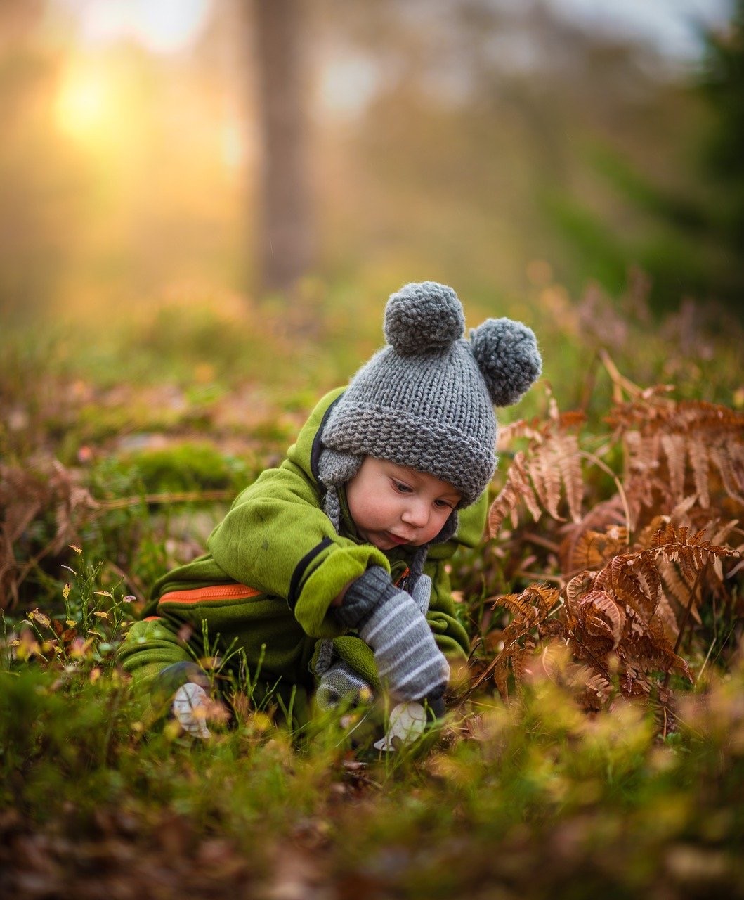 Kleinkind mit Wollmütze spielt im herbstlichen Wald